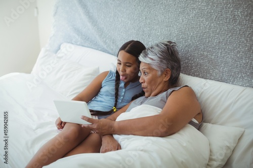 Grandmother and granddaughter using digital tablet in bed room