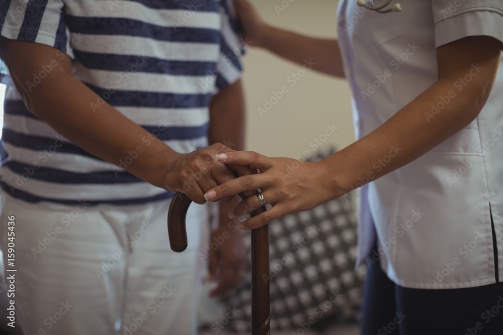 Female doctor helping senior woman to walk with walking stick