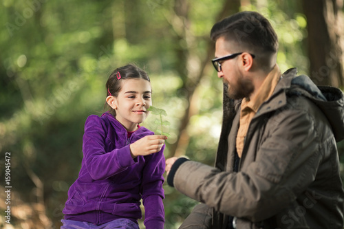 Young father is giving a flower to his cute daughter while hiking in a forest © bokan