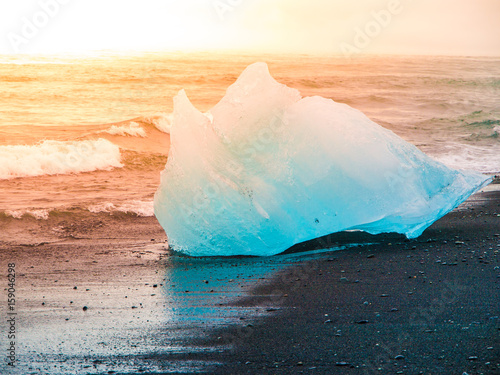 Icebergs sphashed by sea waves on black beach at sunrise time near Jokulsarlon glacier lake, Iceland.