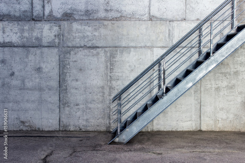 Metallic staircase on the background of gray cement wall - urban minimalist exterior.