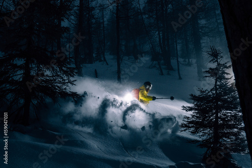 illuminated freerider skiing through dark forest  photo