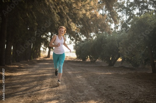 Smiling young woman jogging on dirt road during sunny day