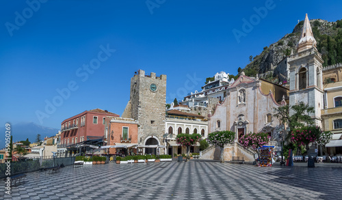 Panoramic view of Taormina main square (Piazza IX Aprile) with San Giuseppe Church, the Clock Tower and Mount Etna Volcano on background - Taormina, Sicily, Italy