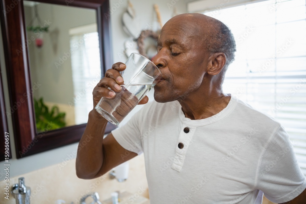 Senior man taking medicine while standing in bathroom Senior man taking medicine while standing in bathroom