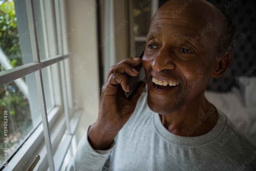 Happy senior man talking on mobile phone by window Happy senior man talking on mobile phone by window
