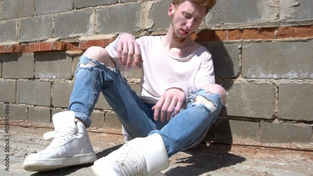 A young red-haired man sits on the roof floor in a hot sunny day A young red-haired man sits on the roof floor in a hot sunny day