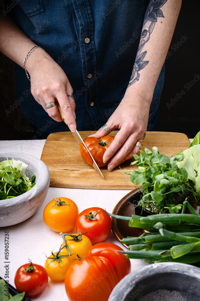 © Darren Muir/Stocksy - Woman slicing tomato on a wooden cutting board