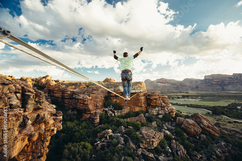 Man balance walking on a highline or tight rope high over a mountain valley at sunset