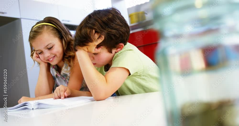 Siblings reading book in kitchen Siblings reading book in kitchen