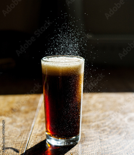 Fizzing glass of cola on wooden table photo