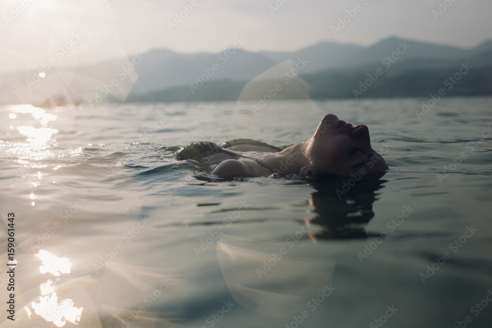 © michela ravasio/Stocksy - Young woman floating in lake at sunset