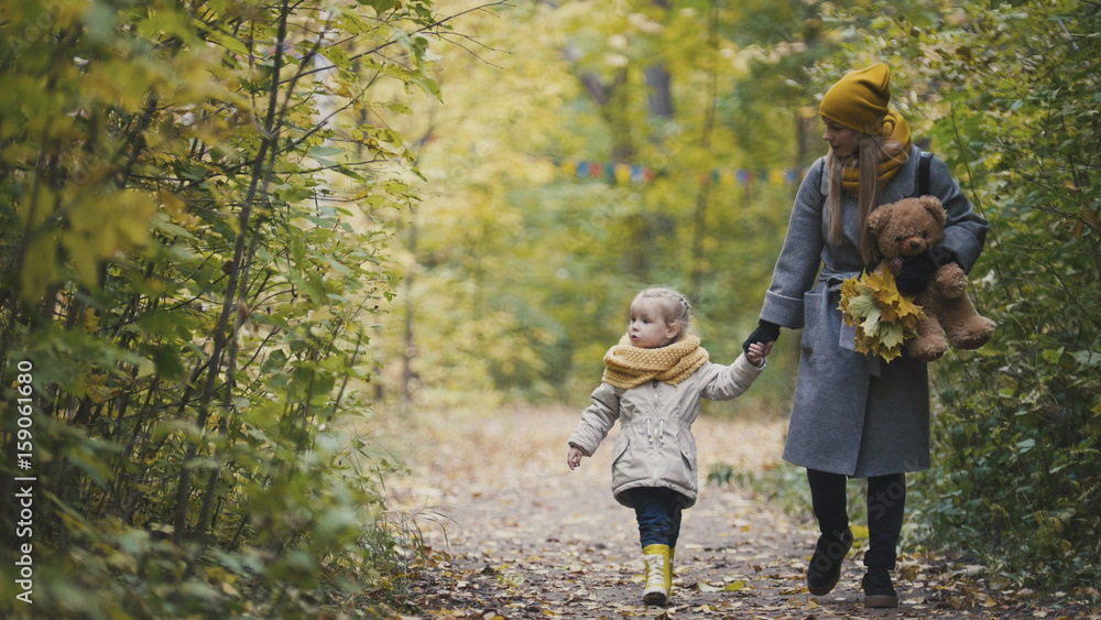 Little daughter with her mother and Teddy Bear walking in autumn park Little daughter with her mother and Teddy Bear walking in autumn park