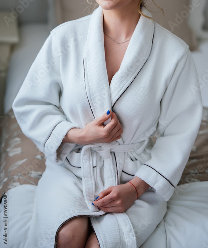 Beautiful slim girl in white robe after shower sitting on bed in the bedroom