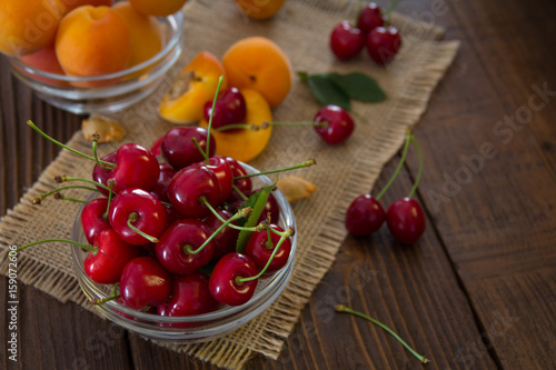 Freshly harvested organic apricots and cherries in bowls on a wooden table