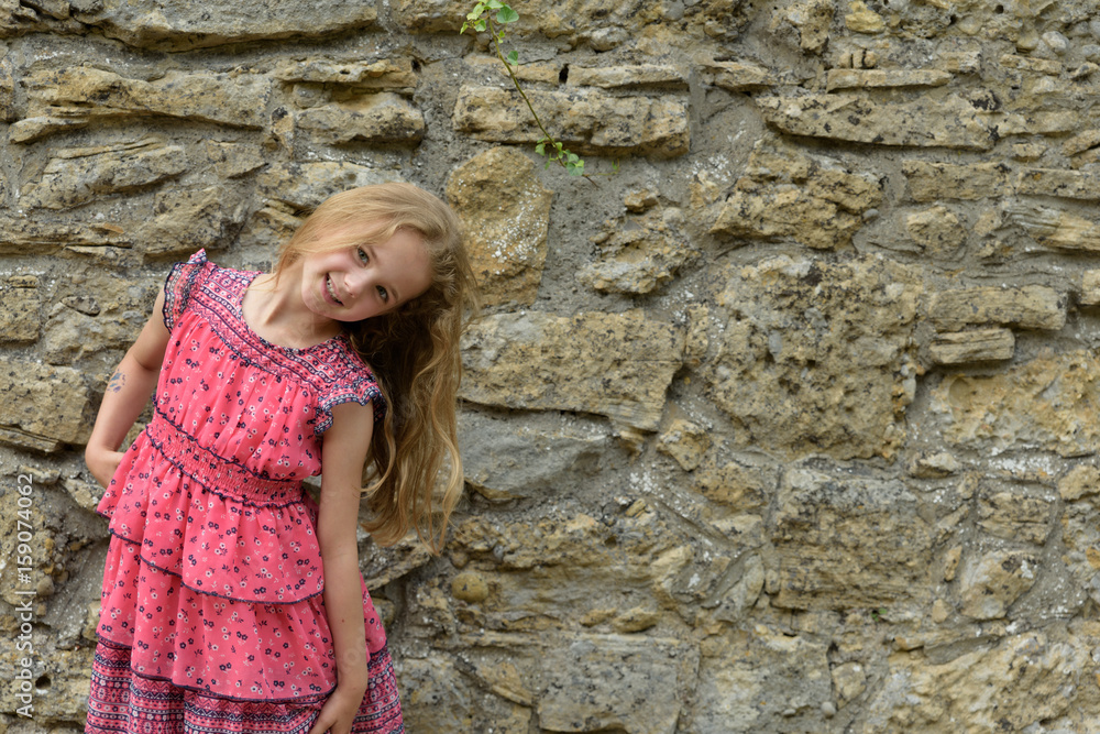 young girl is posing before a old stonewall