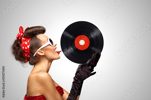 Taste and listen / Beautiful pinup bikini model, licking LP microgroove vinyl record on grey background.