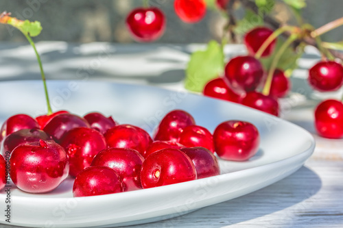 Ripe cherries on a plate and berries on a branch