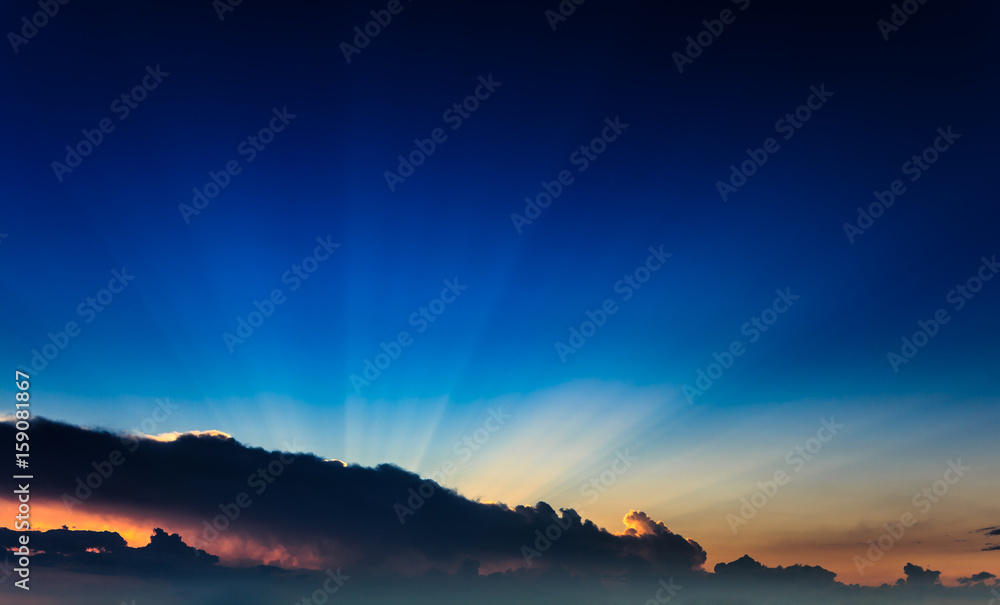 Incredibly, awesome bright, colorful sunset rays become outside a clouds front against the background clear blue sky. Natural phenomenon.