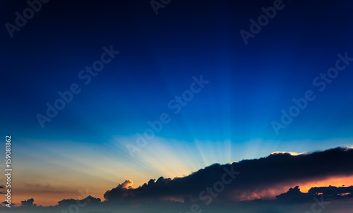 Incredibly, awesome bright, colorful sunset rays become outside a clouds front against the background clear blue sky. Natural phenomenon. © Sodel Vladyslav