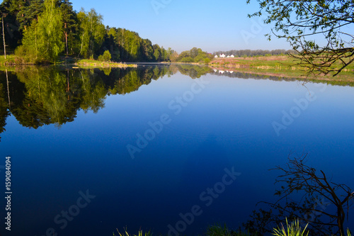 Forest is reflected in the calm blue water of the forest lake. Early morning.