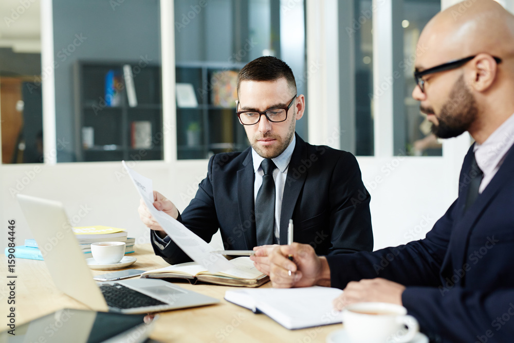 Two confident men discussing financial documents in office Two confident men discussing financial documents in office