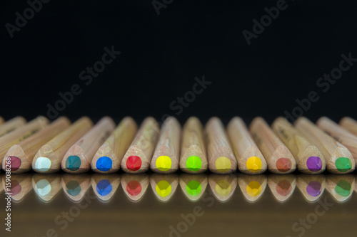 Close-up view of a set of colored pencils lying on a glass mat with reflection and blurred black background