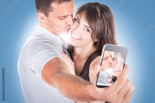 Close-up portrait of beautiful smiling couple hugging and looking at smartphone photo