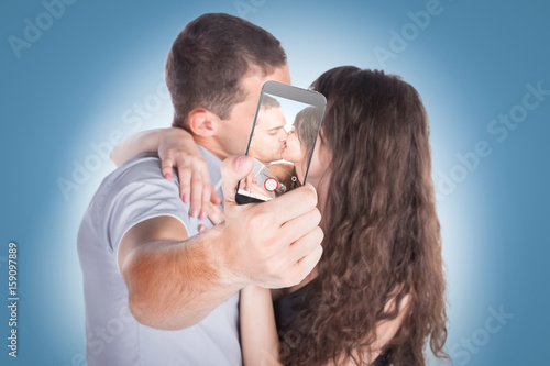 Close-up portrait of beautiful smiling couple hugging and looking at smartphone photo