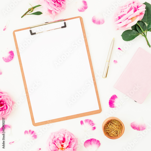 Minimalistic workspace with clipboard, purple roses and accessories on white background. Flat lay, top view. Blogger of freelancer concept