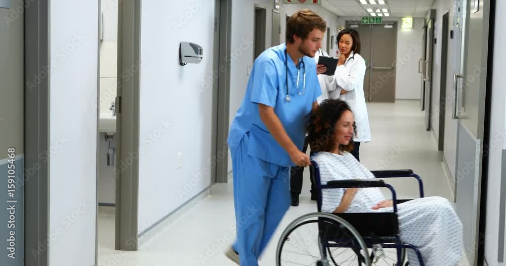 Pregnant woman carrying on wheel chair while doctor discussing in background Pregnant woman carrying on wheel chair while doctor discussing in background