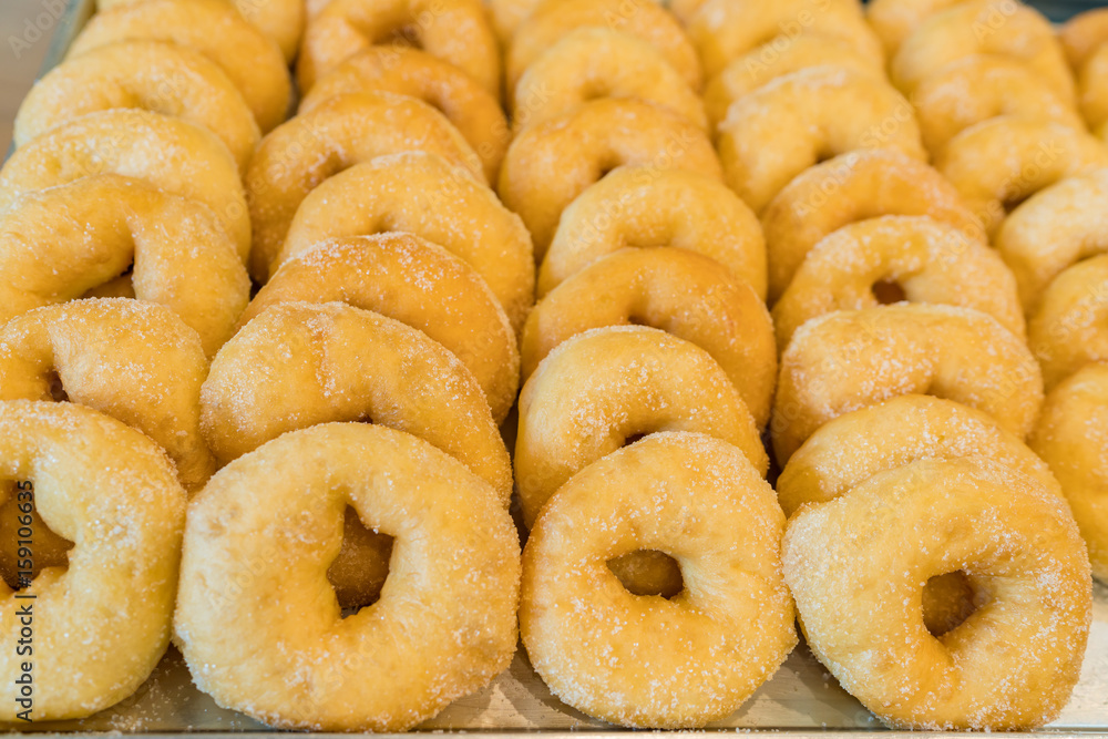 Fresh baked cinnamon donuts staked on a steel tray background.
