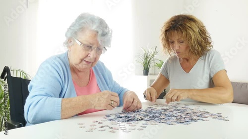 cheerful mature woman doing puzzle and spending time with elderly senior woman at home