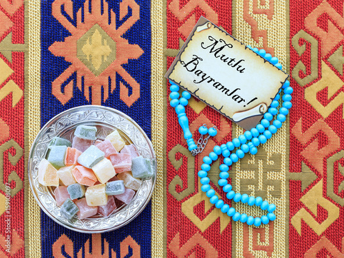 Eid mubarak text in turkish on the card with blue rosary and turkish delights on carpet photo