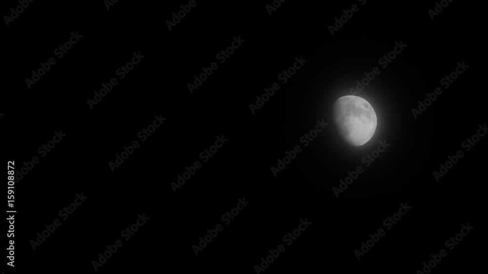 Moon in growing phase on right side blurred by soft clouds. Dark background