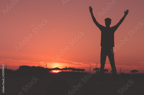 Ragazzo su una balla di fieno con le mani a v di fronte al tramonto