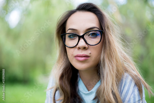 Portrait of a young beautiful woman in glasses, on a green background summer nature.