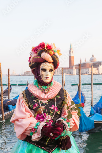 Venice 2017 Carnival, Italy. Woman in colorful costume with rose posing in front of gondolas in the lagoon with San Giorgio Maggiore  visible behind. © gozzoli