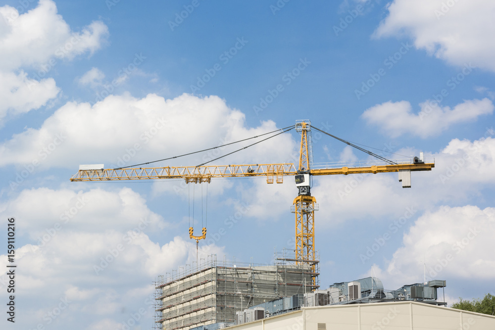 Building crane and top of a building with scaffolding with blue sky and clouds.