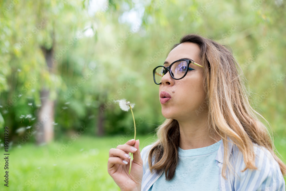 Portrait of beautiful young woman blowing dandelion flower