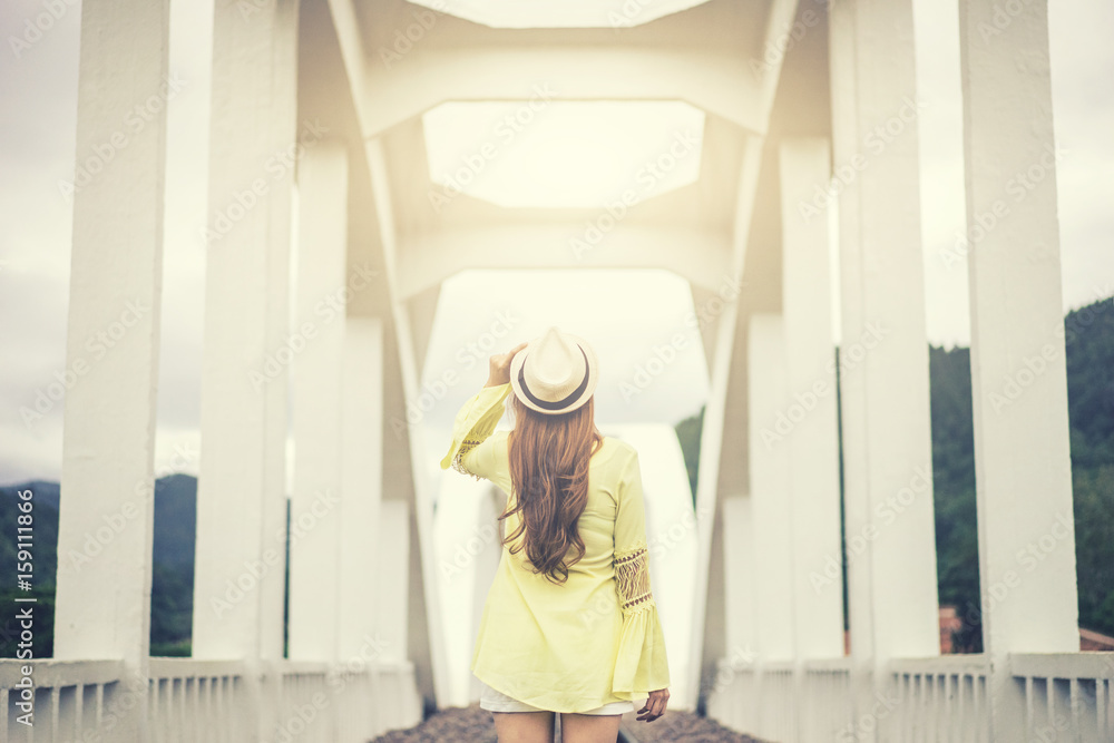 wanderlust young woman holding hat with white bridge background,travel in nature,vacation and relaxation concept.vintage tone and flare effect.