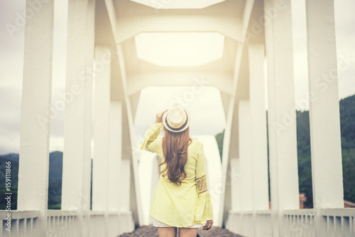 wanderlust young woman holding hat with white bridge background,travel in nature,vacation and relaxation concept.vintage tone and flare effect.