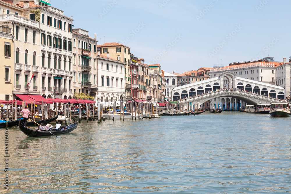 Rialto Bridge, Venice, Veneto,  Italy. Gondolas and vaporettos on the Grand Canal with reflections of historic palazzos in the water