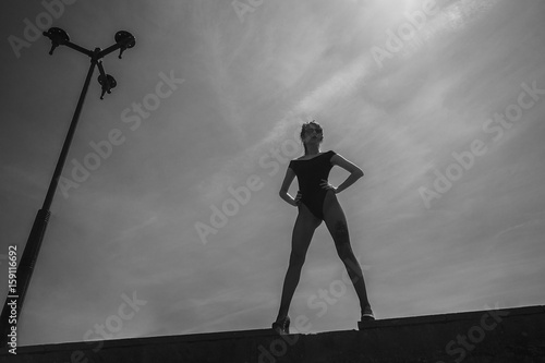 Beautiful young free sexy girl dressed in bodysuit in pantyhose and sunglasses stands in shoes, with a smart ass and long legs against the sky, silhouette of the body © tavrox
