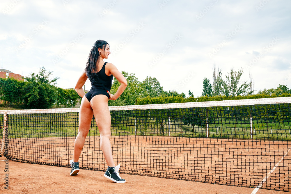 Beautiful young free sports sexy fitness girl dressed in bodysuit, sneakers, with a smart ass and long legs, on a sports ground on a tennis court with a beautiful sky in the background Beautiful young free sports sexy fitness girl dressed in bodysuit, sneakers, with a smart ass and long legs, on a sports ground on a tennis court with a beautiful sky in the background