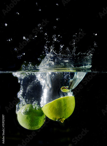 Limes falling in water on black background