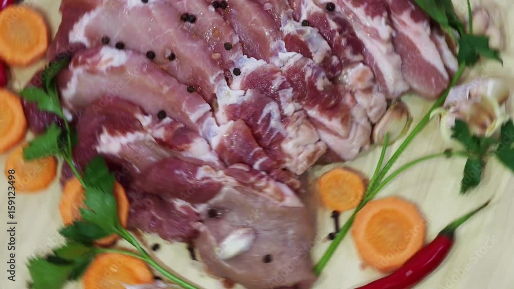 Pieces of raw meat, garlic, pepper, spices and carrot pieces rotate on a tray. Pieces of raw meat, garlic, pepper, spices and carrot pieces rotate on a tray.