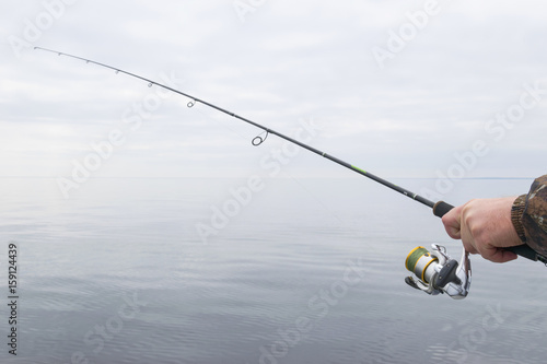 Hands of a fisherman with a spinning rod with the line with a line on a motor boat in the lake on a cloudy day.