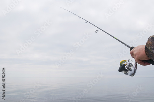 Hands of a fisherman with a spinning rod with the line with a line on a motor boat in the lake on a cloudy day.