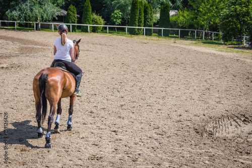 Rear view of female riding a horse in outdoor equestrian arena